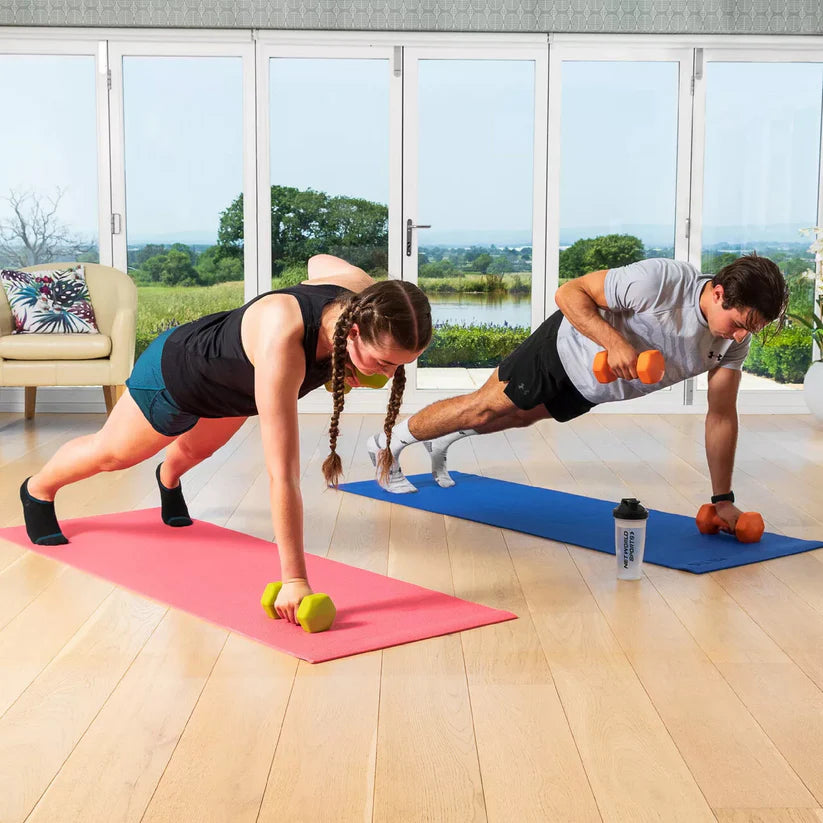 Two people exercising with dumbbells on yoga mats in a bright room with large windows.